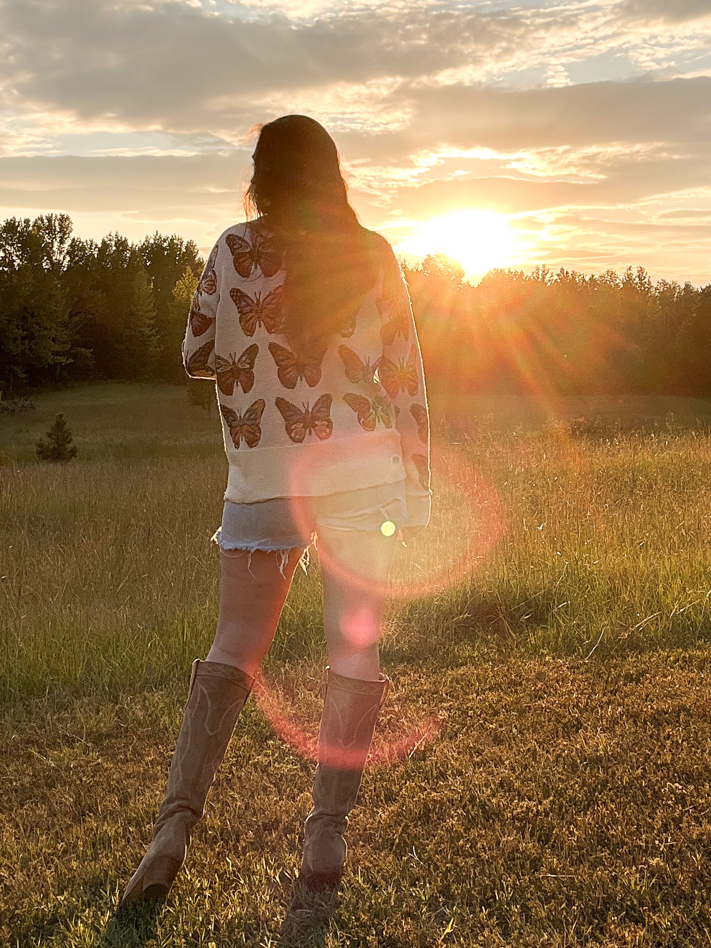 Pictures from the back, Merino Wool Cardigan in Milky White with butterflies in shades of red, blue, tangerine, and black.  Made in family owned factory in Italy. Worn with denim cutoff shorts and cowboy boots.