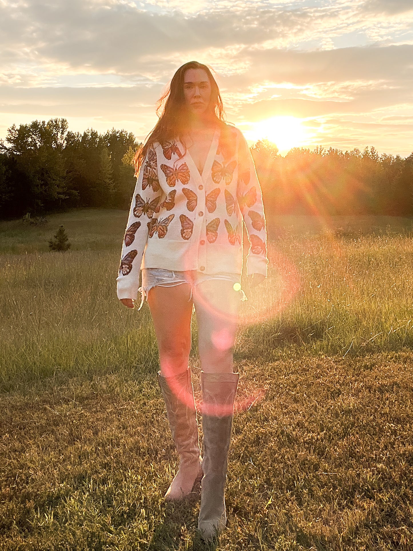 Full front view of Merino Wool Cardigan in Milky White with butterflies in shades of red, blue, tangerine, and black.  Made in family owned factory in Italy. Worn with denim cutoff shorts and cowboy boots.