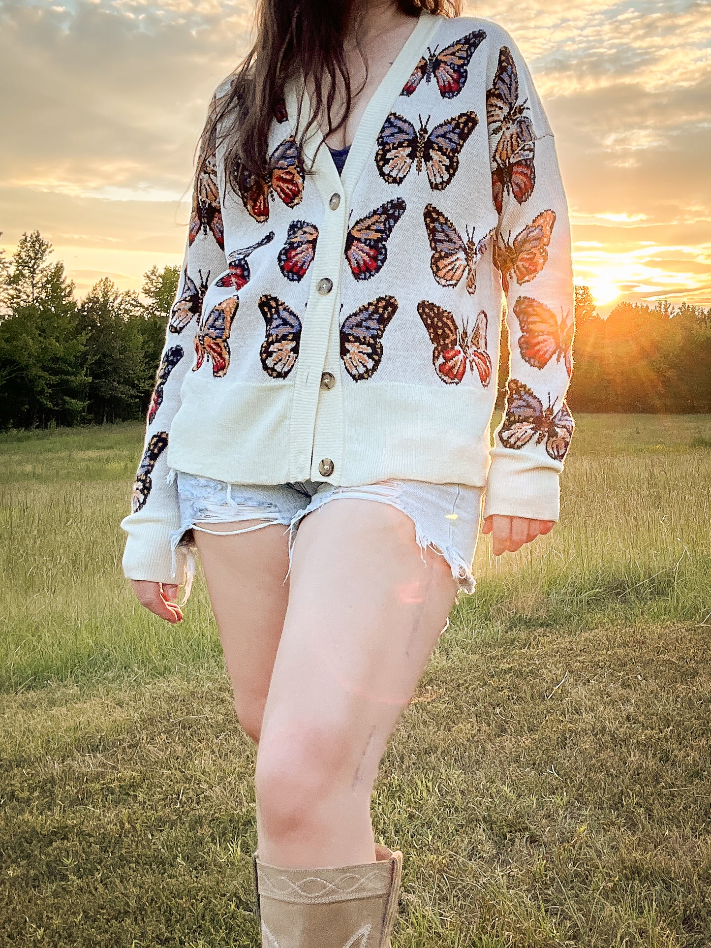 Closer view of Merino Wool Cardigan in Milky White with butterflies in shades of red, blue, tangerine, and black.  Made in family owned factory in Italy. Worn with denim cutoff shorts and cowboy boots.